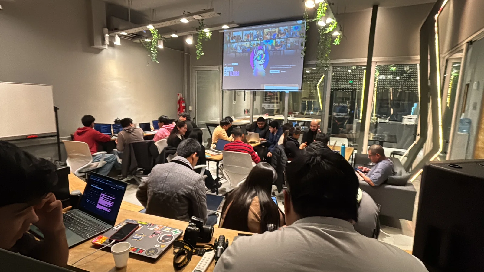 Sala de un meetup con la pantalla Código con altura y gente trabajando en notebooks
