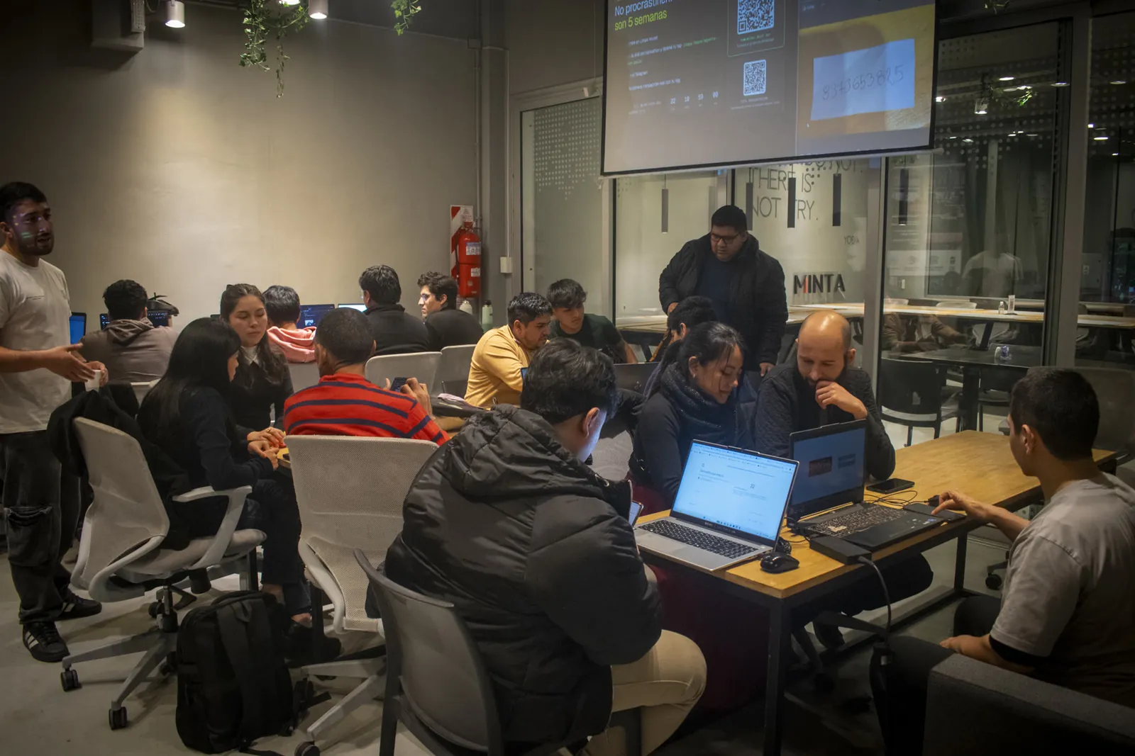 Grupo trabajando en MINTA durante un meetup, con la pantalla No procrastinar y alguien de pie